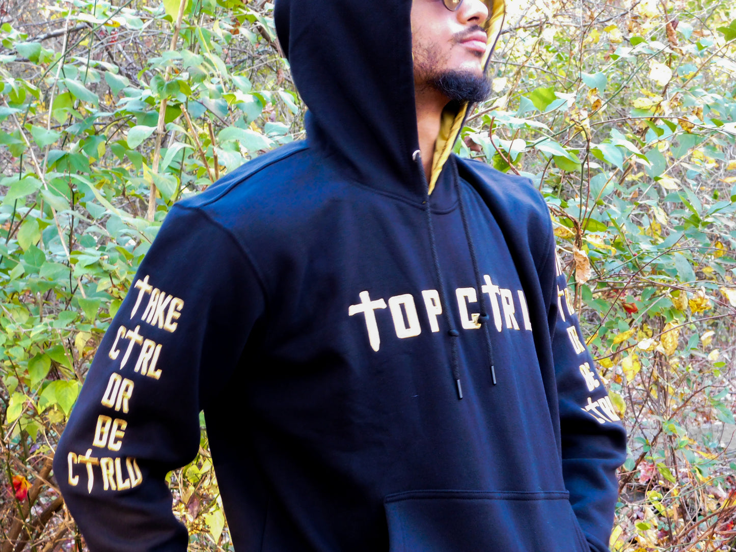 Person wearing a black and gold hoodie with text in an outdoor setting.