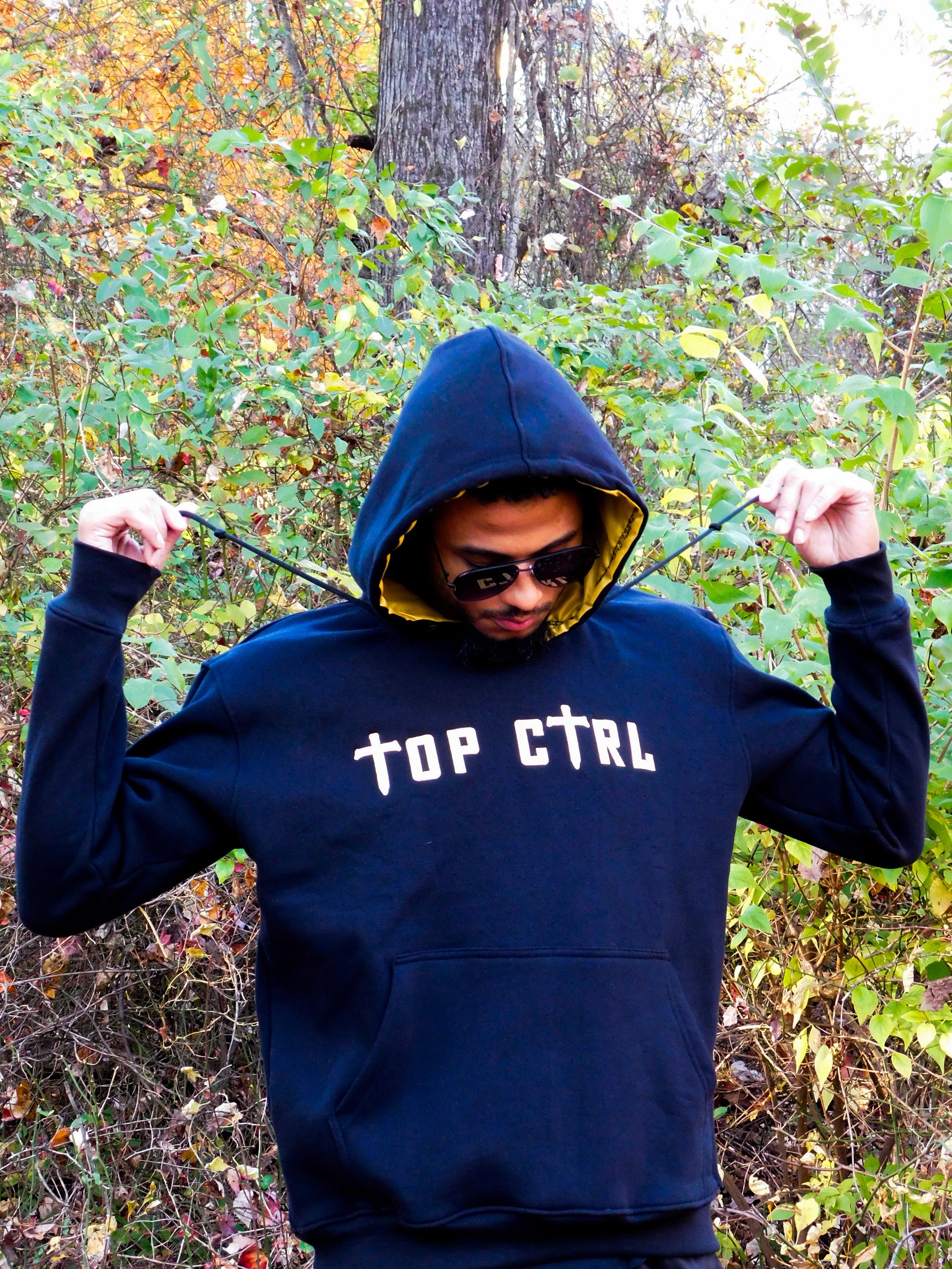 Person wearing a black and gold hoodie with 'TOP CTRL' text in an outdoor setting.