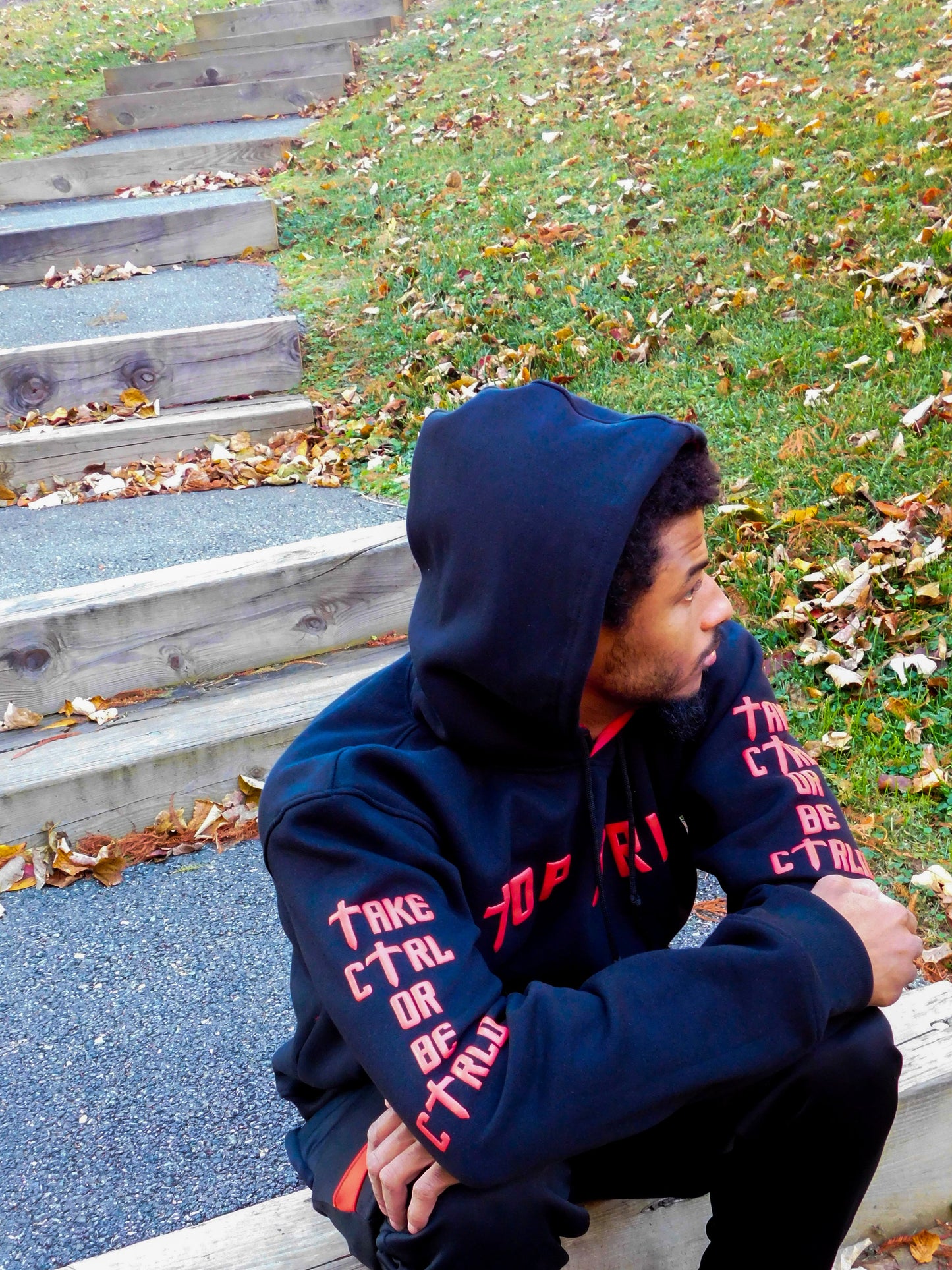 Person wearing a black and red hoodie with text, sitting on steps with grass and leaves in the background