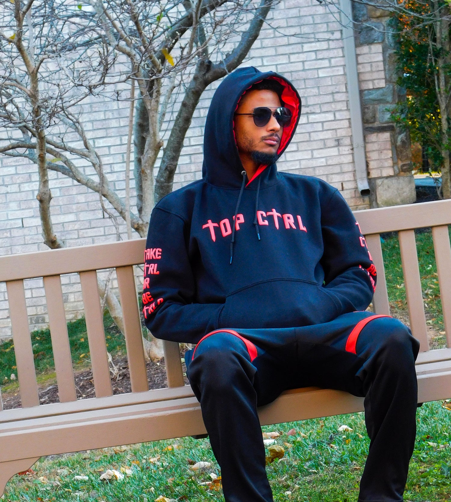 Person wearing a dark hoodie with 'TOP CTRL' text, sitting on a bench outdoors.